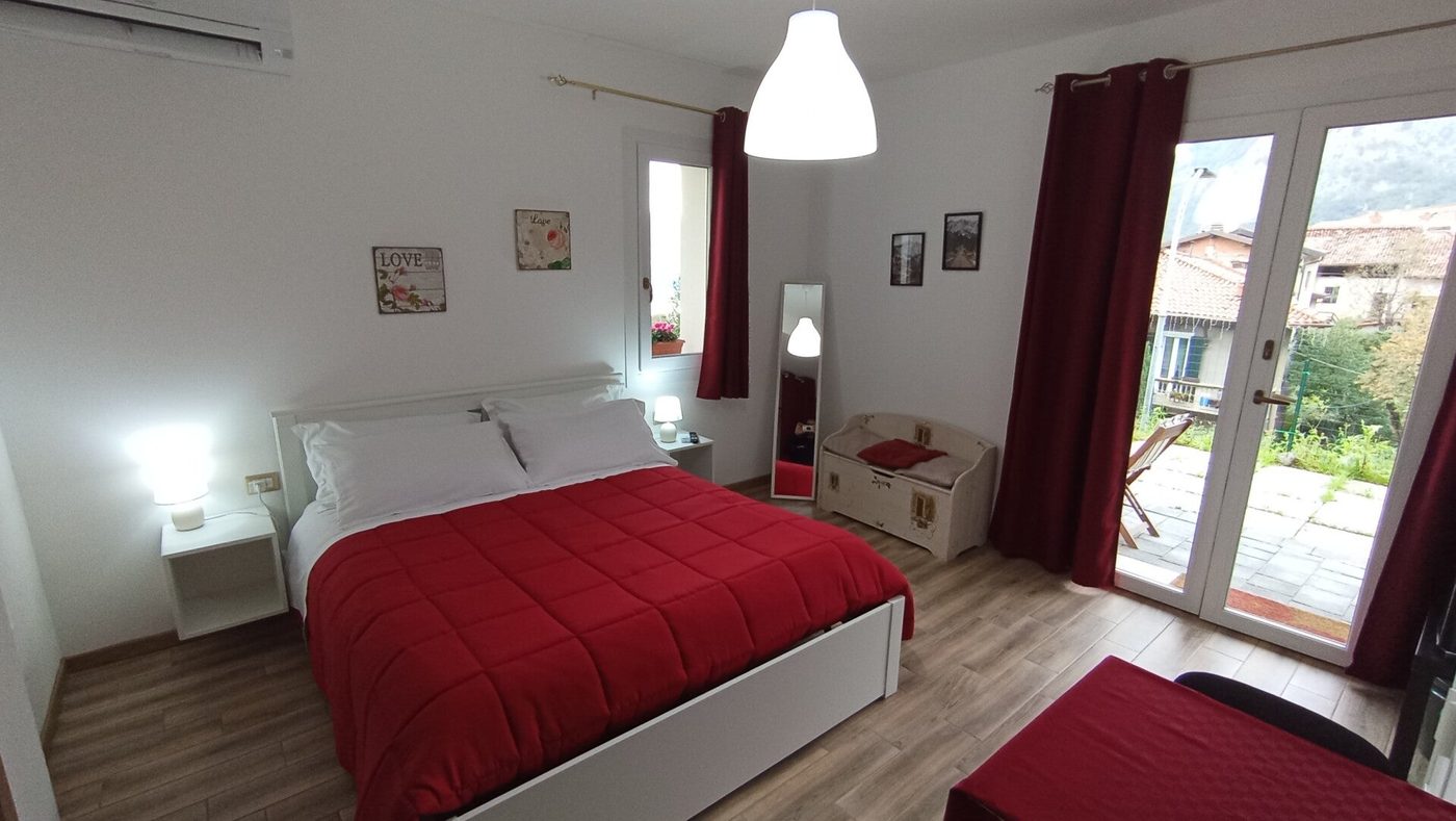 Camera 1: letto matrimoniale con copriletto rosso e porta finestra sulla terrazza